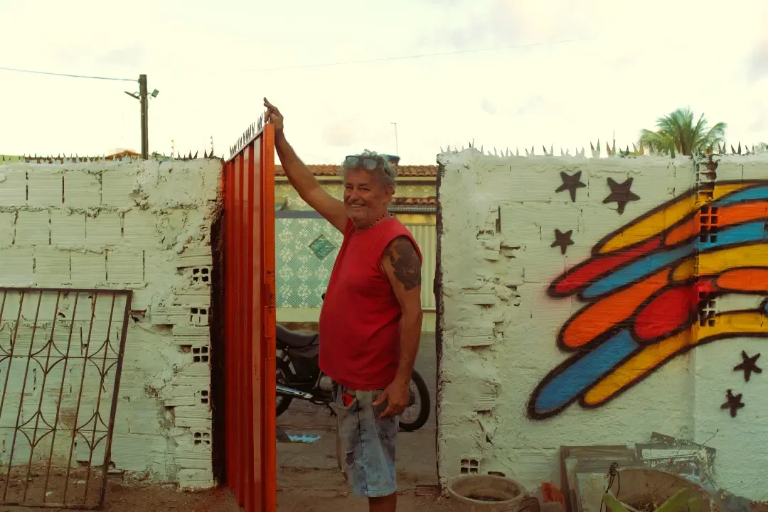 Integrante do coletivo abre o portão laranja da sede, ao lado de um muro grafitado